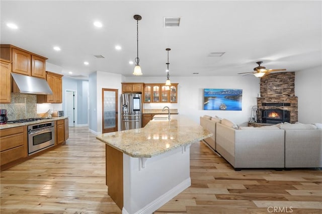 kitchen with appliances with stainless steel finishes, tasteful backsplash, decorative light fixtures, a kitchen island with sink, and sink