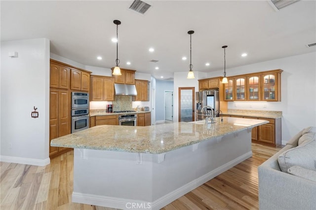 kitchen featuring range hood, pendant lighting, appliances with stainless steel finishes, a breakfast bar area, and a large island