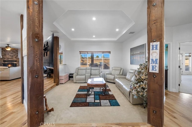 living room with ceiling fan, a fireplace, light hardwood / wood-style flooring, and a tray ceiling