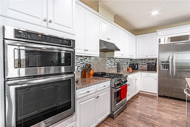 kitchen featuring premium appliances, white cabinets, dark hardwood / wood-style flooring, dark stone counters, and decorative backsplash