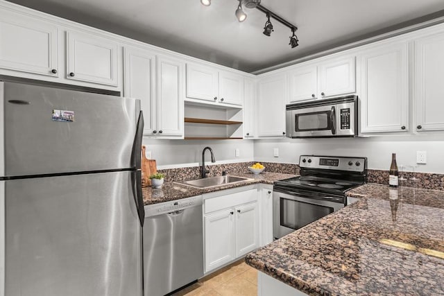 kitchen with appliances with stainless steel finishes, white cabinetry, dark stone countertops, sink, and light tile patterned flooring