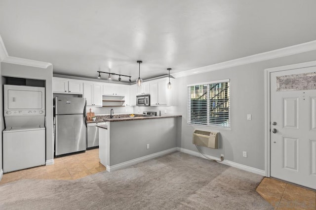 kitchen featuring pendant lighting, kitchen peninsula, stacked washer and dryer, appliances with stainless steel finishes, and white cabinets