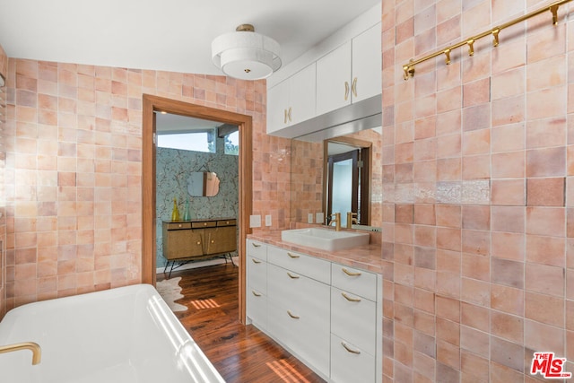 bathroom featuring vaulted ceiling, tile walls, hardwood / wood-style flooring, a washtub, and vanity