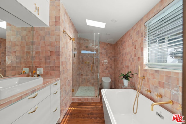 full bathroom with tile walls, independent shower and bath, vanity, and toilet