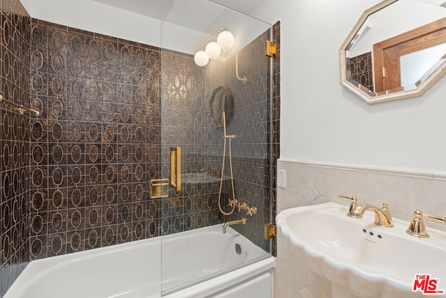 bathroom with tile walls, bath / shower combo with glass door, and sink