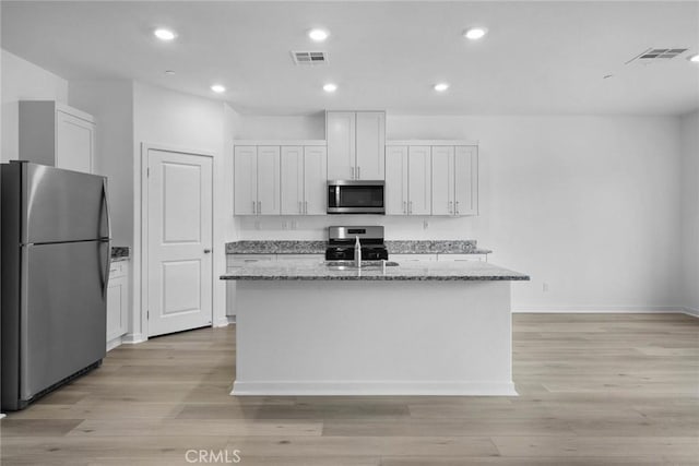 kitchen featuring light stone counters, white cabinetry, appliances with stainless steel finishes, and a center island with sink