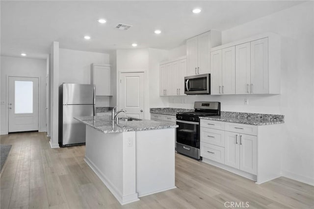 kitchen with sink, white cabinetry, appliances with stainless steel finishes, an island with sink, and light stone counters