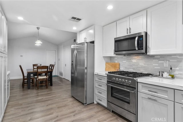 kitchen featuring lofted ceiling, tasteful backsplash, white cabinetry, stainless steel appliances, and light stone counters