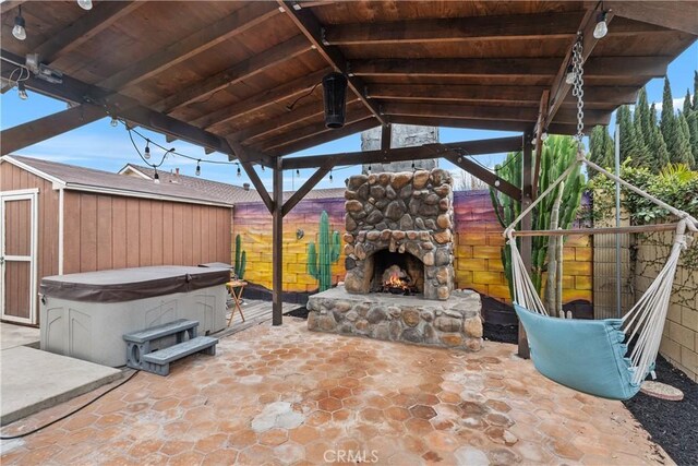 view of patio with an outdoor stone fireplace, a hot tub, and a storage unit