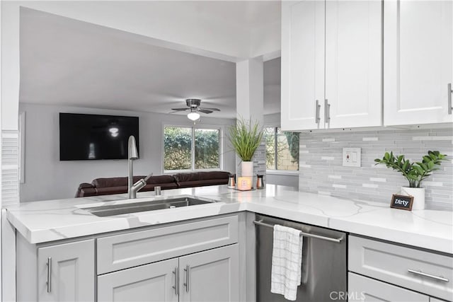 kitchen featuring kitchen peninsula, stainless steel dishwasher, white cabinets, light stone counters, and sink