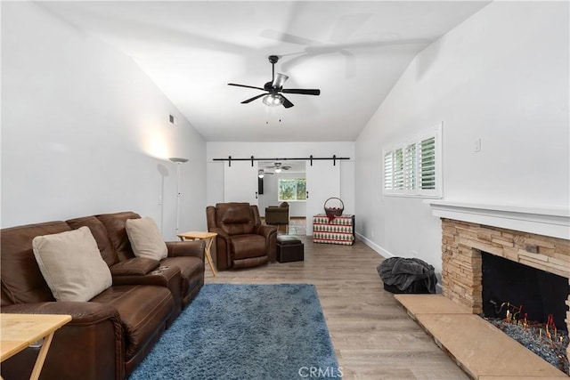 living room featuring vaulted ceiling, ceiling fan, light wood-type flooring, and a stone fireplace