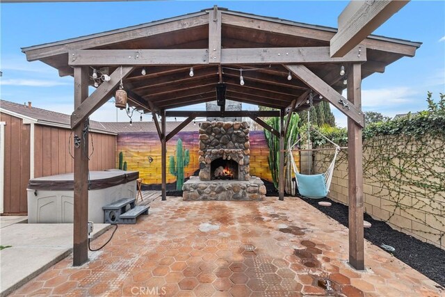 view of patio with a gazebo, a hot tub, and an outdoor stone fireplace