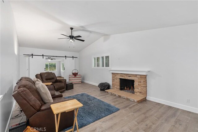 living room with ceiling fan, vaulted ceiling, a stone fireplace, and hardwood / wood-style floors