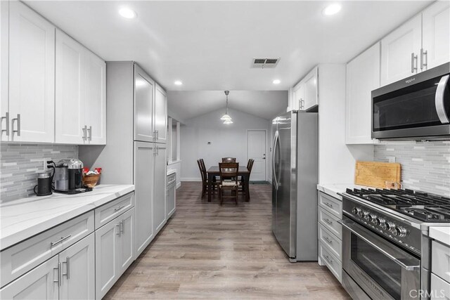 kitchen with white cabinetry, stainless steel appliances, lofted ceiling, hanging light fixtures, and light stone counters