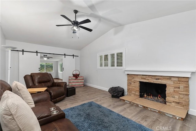 living room with ceiling fan, wood-type flooring, vaulted ceiling, and a stone fireplace