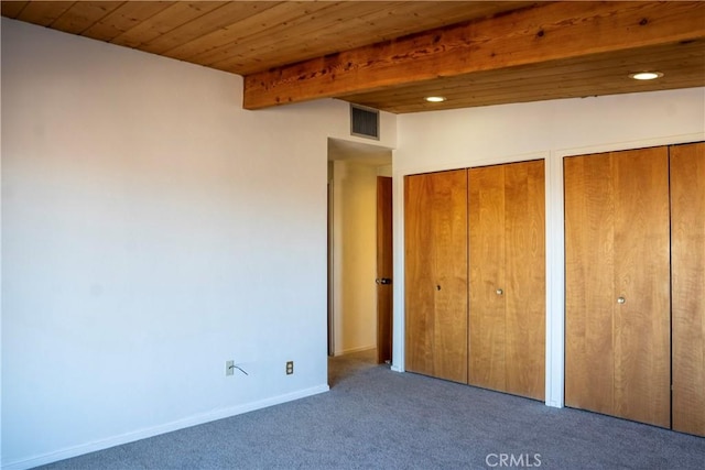 unfurnished bedroom featuring carpet, beam ceiling, multiple closets, and wood ceiling