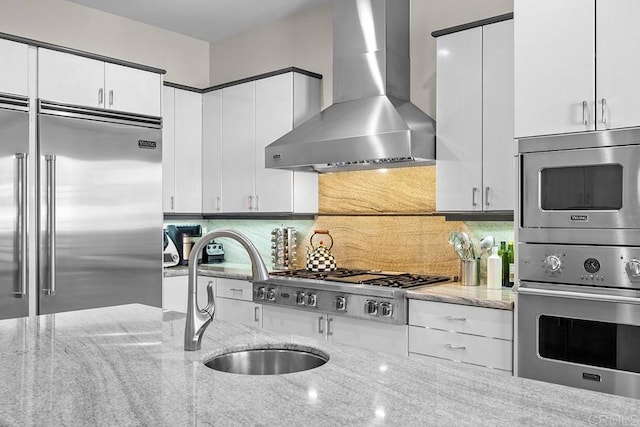 kitchen with white cabinets, sink, wall chimney range hood, and built in appliances