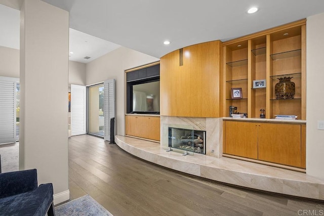 living room with built in shelves, a high end fireplace, and light wood-type flooring