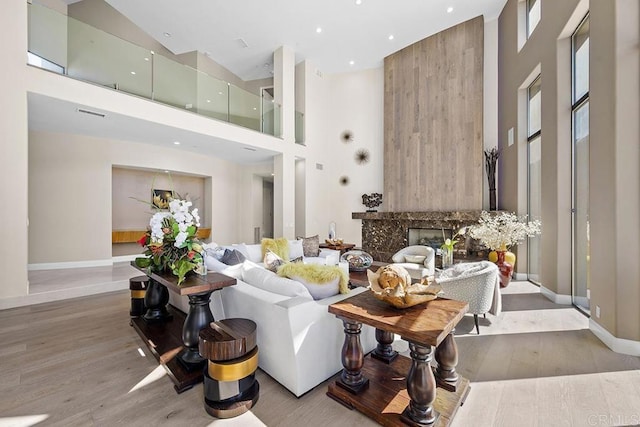 living room with a high end fireplace, light hardwood / wood-style flooring, and a high ceiling