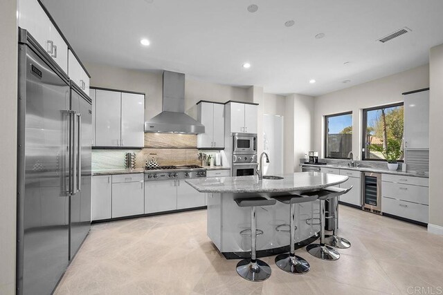 1107 Majestad Ln, Chula Vista, CA 91910 - kitchen with built in appliances, wine cooler, wall chimney exhaust hood, visible vents, and white cabinets