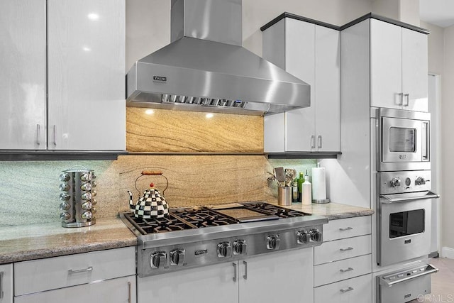 kitchen with decorative backsplash, a warming drawer, white cabinetry, wall chimney range hood, and appliances with stainless steel finishes