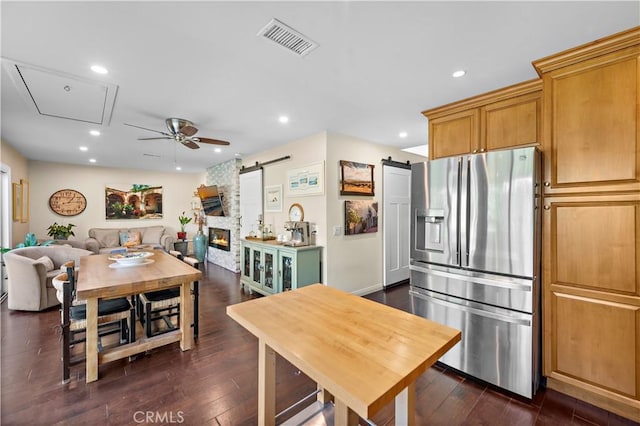 kitchen with stainless steel refrigerator with ice dispenser, ceiling fan, a barn door, and dark wood-type flooring