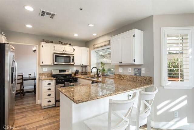 kitchen with white cabinetry, stainless steel appliances, sink, kitchen peninsula, and light hardwood / wood-style flooring