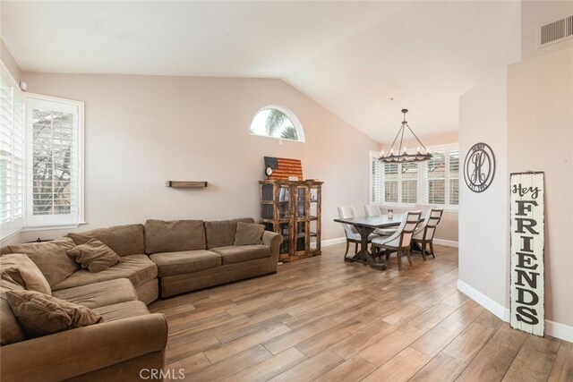 living room featuring light hardwood / wood-style floors, an inviting chandelier, a healthy amount of sunlight, and vaulted ceiling