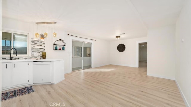 interior space with white cabinets, decorative light fixtures, light hardwood / wood-style floors, sink, and white dishwasher