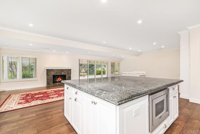 kitchen featuring stainless steel microwave, dark hardwood / wood-style flooring, a high end fireplace, white cabinets, and a center island