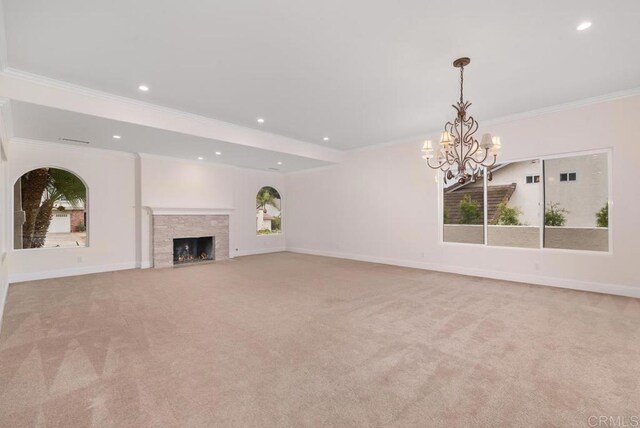 unfurnished living room featuring ornamental molding, light carpet, a stone fireplace, and an inviting chandelier