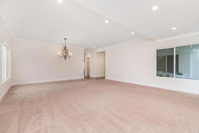 spare room featuring light carpet, ornamental molding, and a chandelier