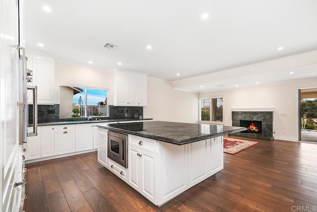 kitchen featuring stainless steel microwave, dark hardwood / wood-style flooring, white cabinets, and tasteful backsplash