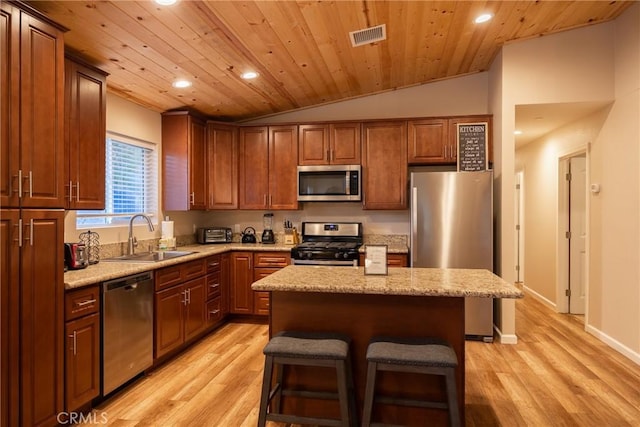 kitchen featuring appliances with stainless steel finishes, a center island, light hardwood / wood-style floors, sink, and vaulted ceiling