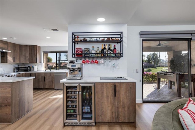 bar with appliances with stainless steel finishes, wine cooler, sink, light hardwood / wood-style flooring, and dark brown cabinets