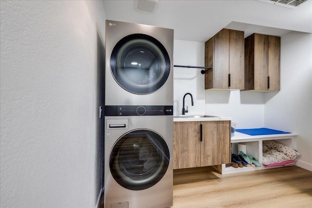 laundry room featuring stacked washer / dryer, sink, light hardwood / wood-style floors, and cabinets