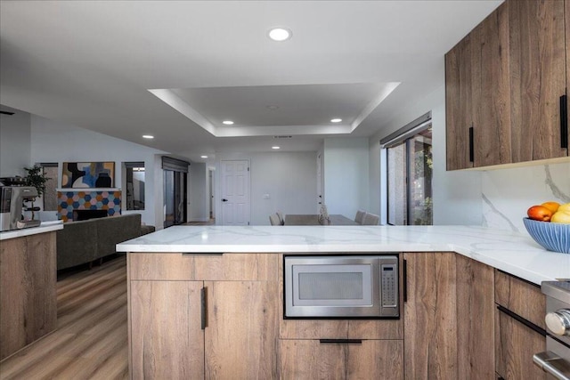 kitchen with light stone countertops, stainless steel appliances, kitchen peninsula, light wood-type flooring, and a tiled fireplace