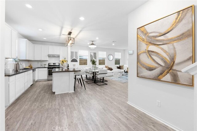 kitchen with white cabinets, a center island, stainless steel appliances, tasteful backsplash, and light wood-type flooring