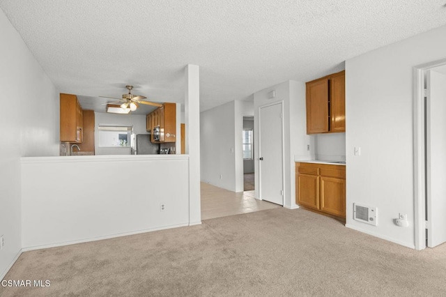 unfurnished living room with ceiling fan, light colored carpet, and a textured ceiling