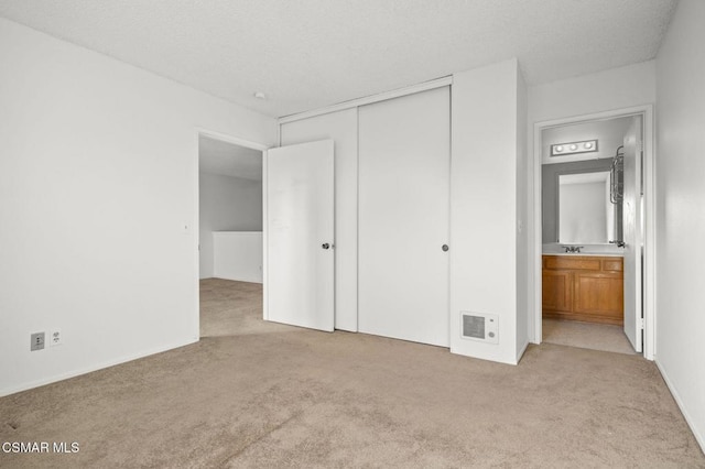 unfurnished bedroom featuring a closet, ensuite bathroom, and light colored carpet