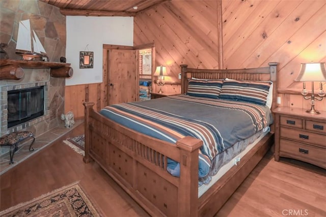 bedroom with light hardwood / wood-style floors, a stone fireplace, and wood ceiling