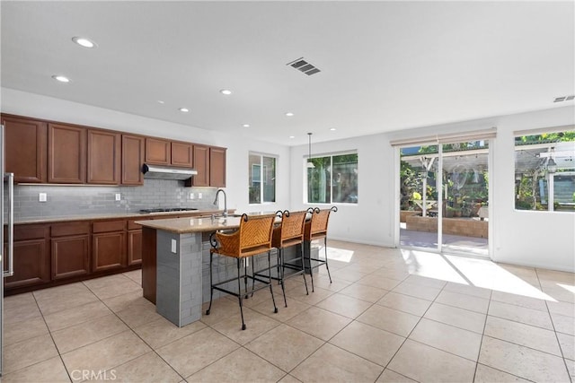 kitchen with stainless steel gas cooktop, a kitchen island with sink, light tile patterned flooring, and a breakfast bar area