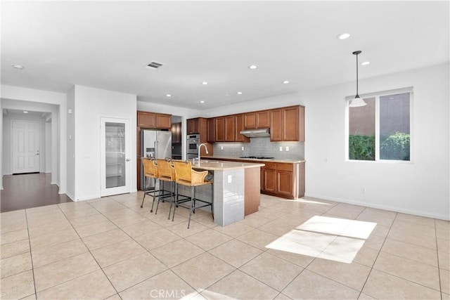 kitchen with tasteful backsplash, an island with sink, sink, hanging light fixtures, and a breakfast bar area