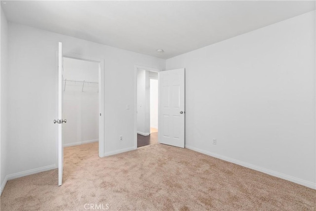 unfurnished bedroom with a walk in closet, a closet, and light carpet