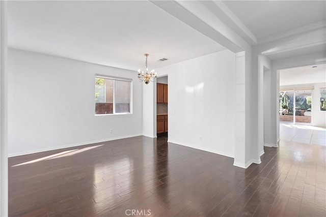 empty room with plenty of natural light, dark hardwood / wood-style floors, and a chandelier