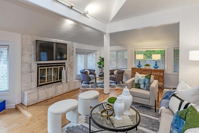 living room with a tiled fireplace, vaulted ceiling, and hardwood / wood-style flooring