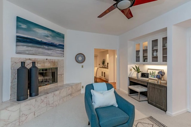 sitting room with ceiling fan, a tiled fireplace, and light colored carpet