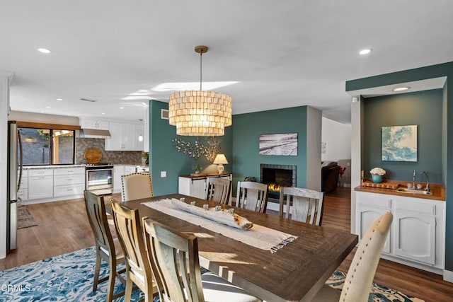 dining room featuring hardwood / wood-style floors, a notable chandelier, sink, and a brick fireplace