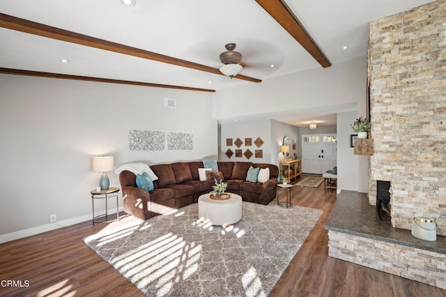 living room with beam ceiling, a stone fireplace, ceiling fan, and dark wood-type flooring