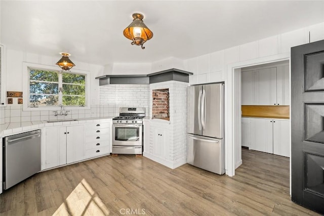 kitchen featuring white cabinetry, light hardwood / wood-style floors, appliances with stainless steel finishes, hanging light fixtures, and sink